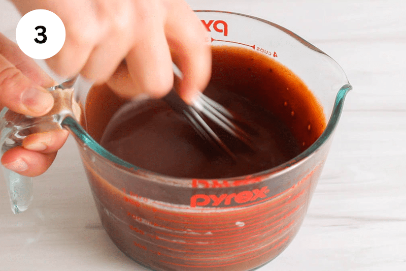 A small whisk stirring a chocolate sauce in a glass jar.