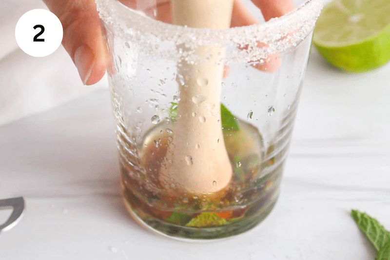 A muddler crushing mint leaves at the bottom of a glass.