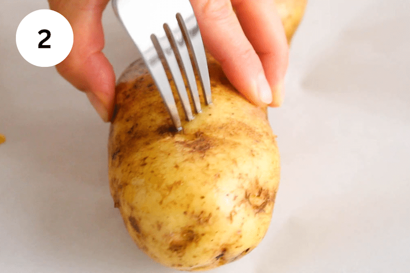 A fork poking holes in a potato.