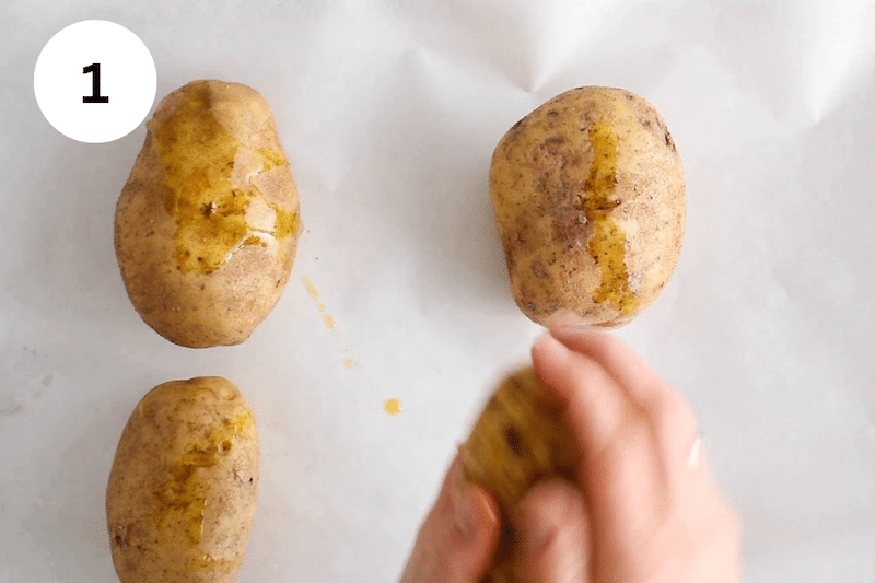 Hands rubbing olive oil over Russet potatoes.