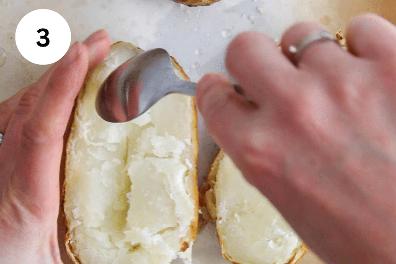 A spoon emptying out the flesh from a baked potato.