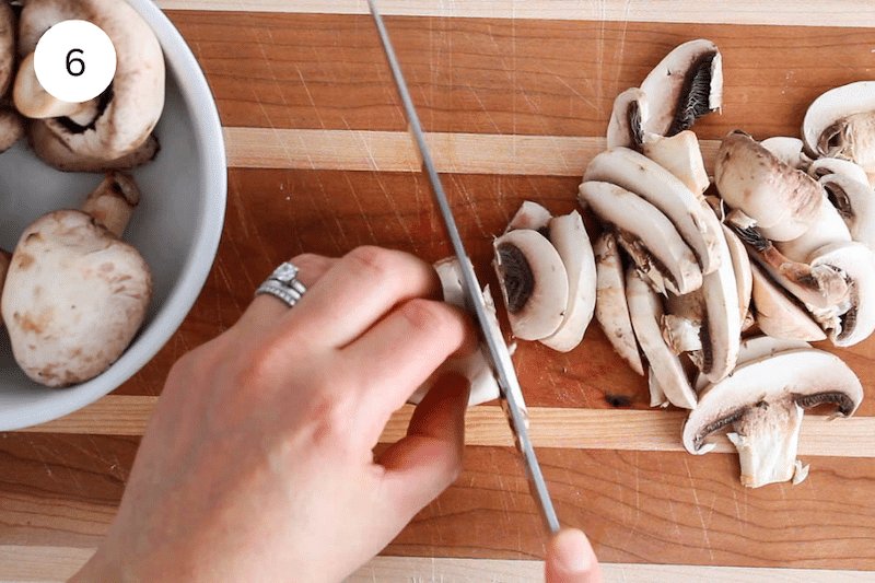 A large knife slicing mushrooms on a cutting.