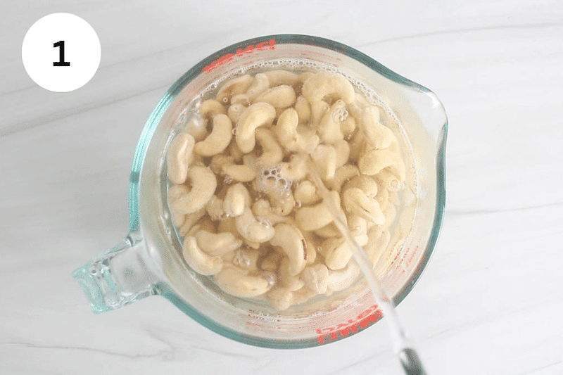 Boiling water pouring over a container filled with raw cashews.