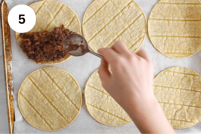 A spoon adding black bean filling over corn tortilla.