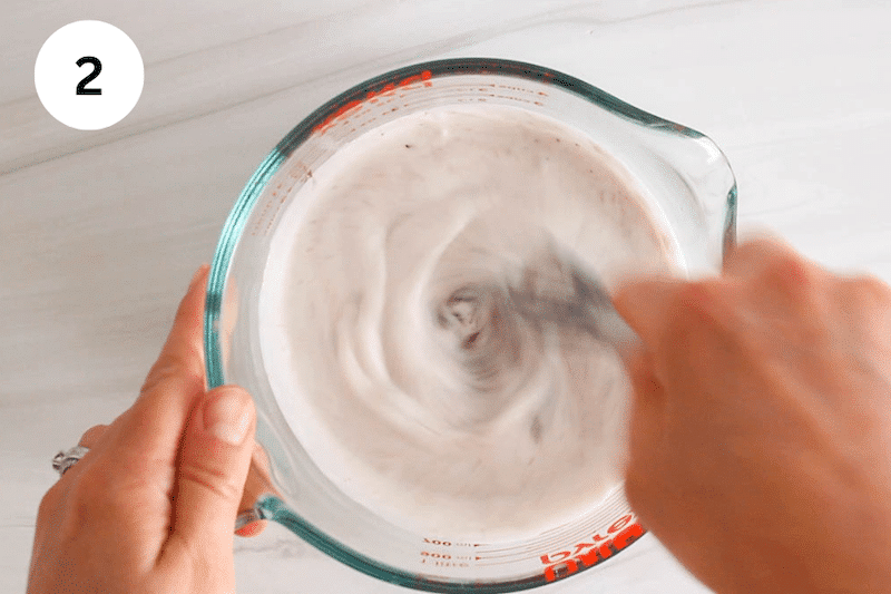 A small whisk stirring a coconut milk and chocolate mixture.