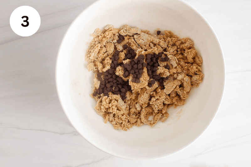 A white bowl with cookie dough and chocolate chips over.