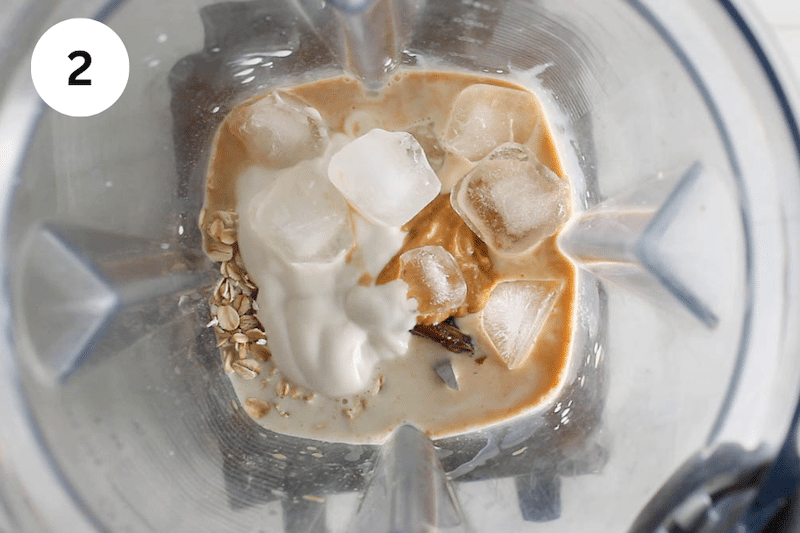 Milk, peanut butter, yogurt and oats in a blender topped with ice cubes.