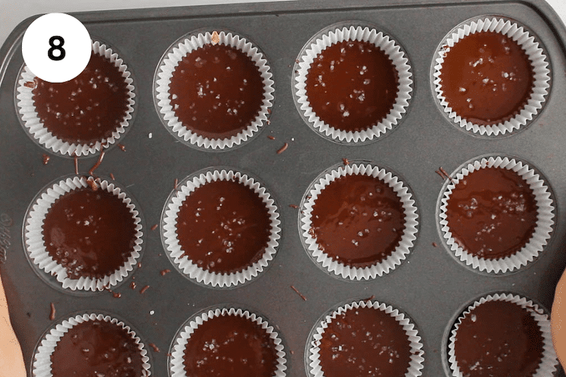 A muffin pan filled with chocolate cups garnished with sea salt.