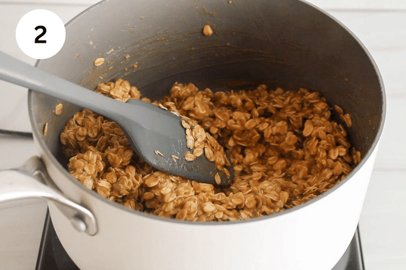 A spatula stirring a sticky oat mix in a saucepan.