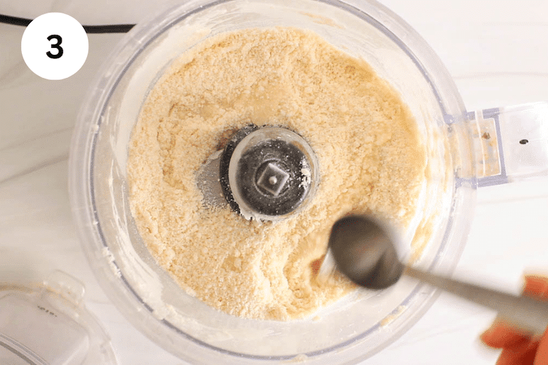 A spoon adding water to a food processor.