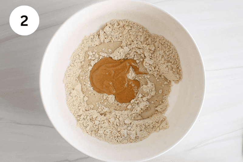 A white bowl with a flour mixture and milk and peanut butter over.