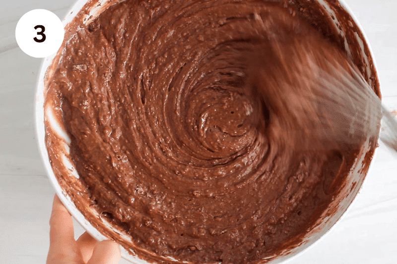 A large whisk mixing a chocolate cake batter.