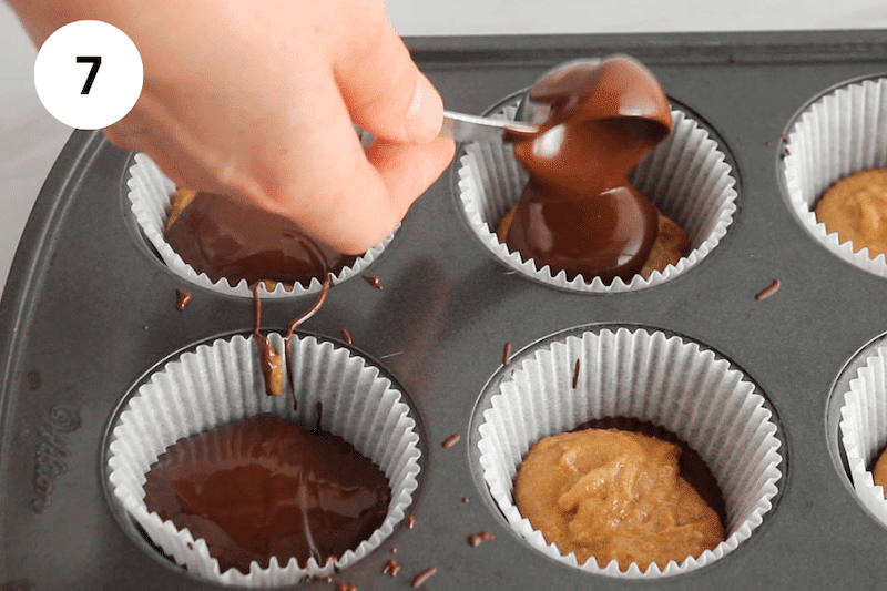 A spoon adding chocolate to muffin liners.