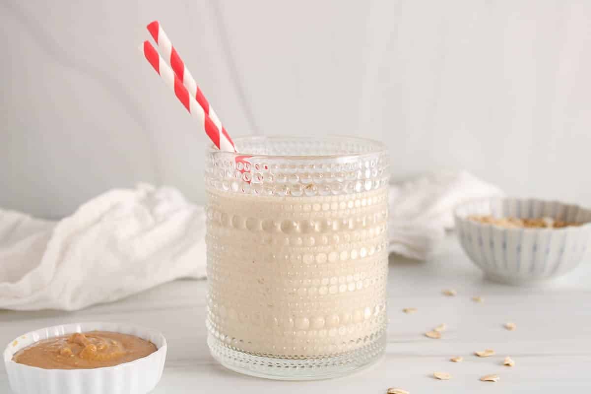 A short glass filled with a no banana peanut butter oatmeal smoothie and a red and white straw.