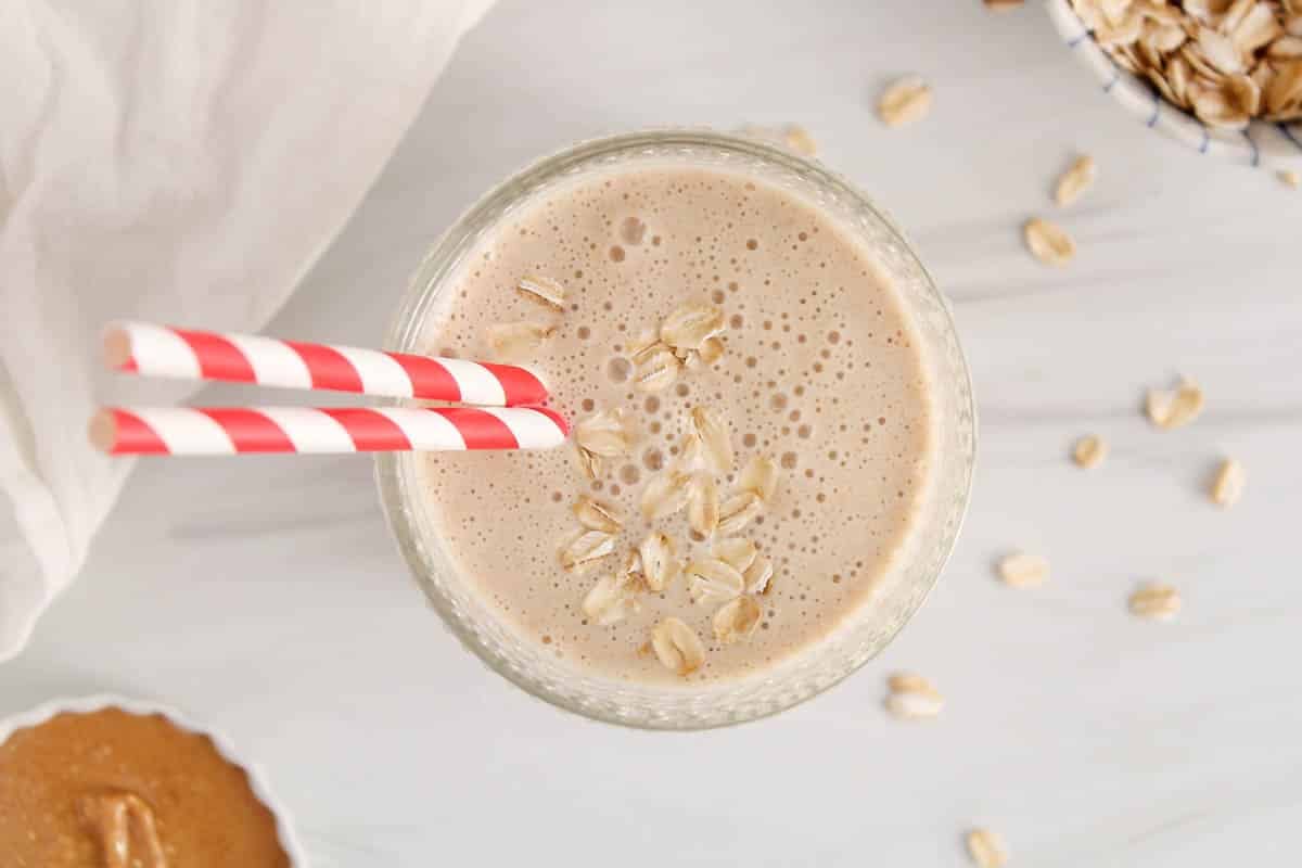 A short glass filled with a peanut butter smoothie made without banana and covered with rolled oats.