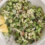 Large bowl filled with a broccoli crunch salad and a side of lemon wedges.