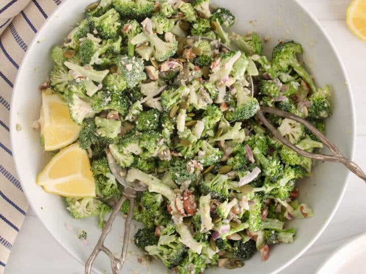 Large bowl filled with a broccoli crunch salad and a side of lemon wedges.