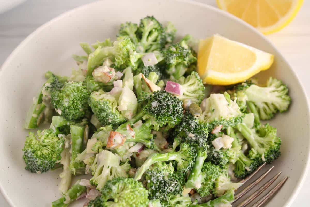 A portion of broccoli crunch salad with a side of lemon wedge on a small plate.