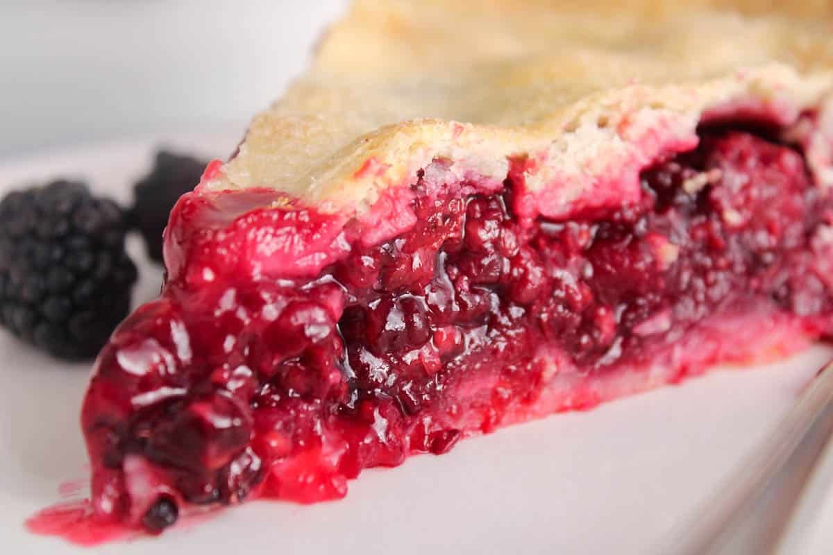 A gooey blackberry filling coming out of a slice of vegan blackberry pie.