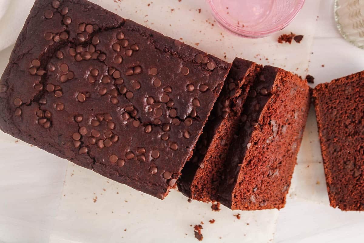 A vegan double chocolate loaf cake half sliced and covered with chocolate chips.