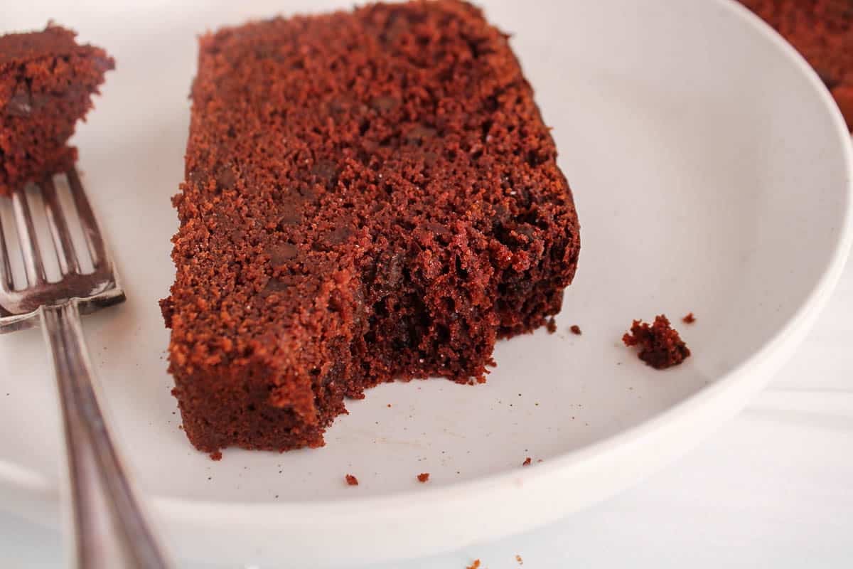 A slice of vegan chocolate loaf cake on a white plate with a bite taken off.