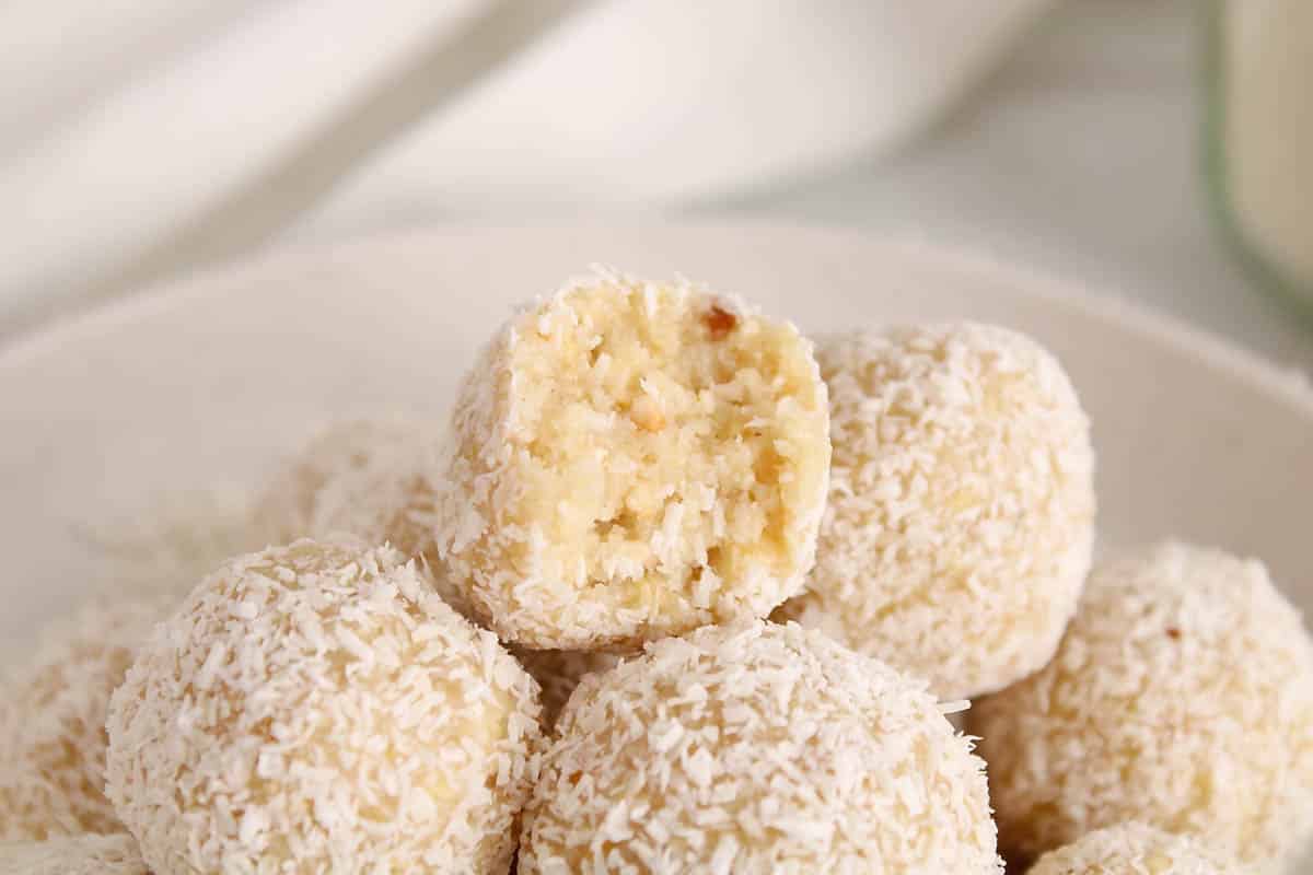A lemon bliss balls with a bite taken off on a pile of many bliss balls.