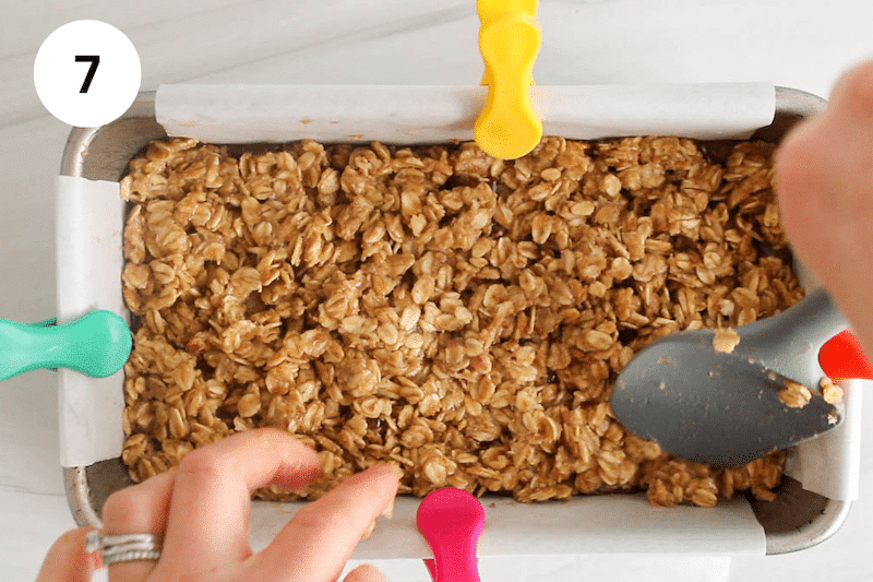 A spatula pressing a oat mix at the bottom of a loaf pan.