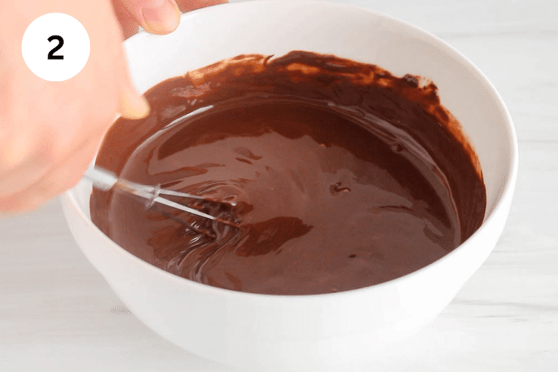 A bowl with a small whisk stirring melted chocolate.