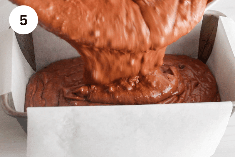 A chocolate cake batter pouring in a loaf pan.