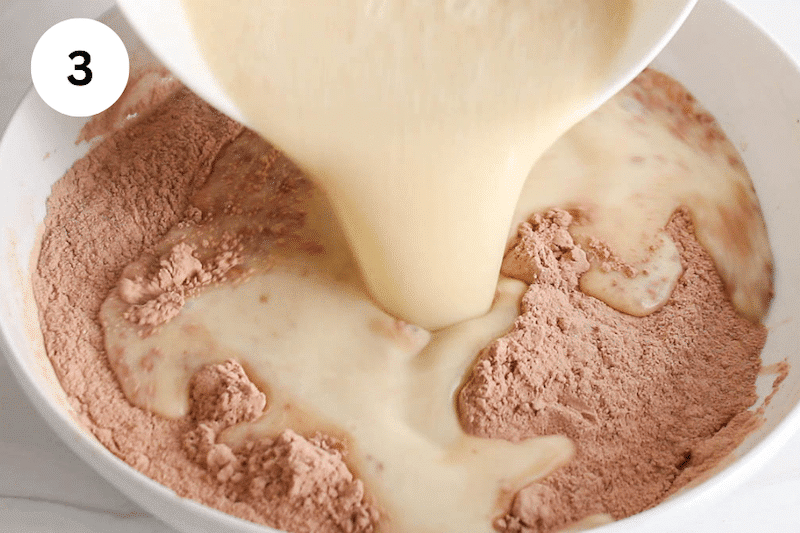 A milk mixture pouring over dry ingredient with flour in a large bowl.