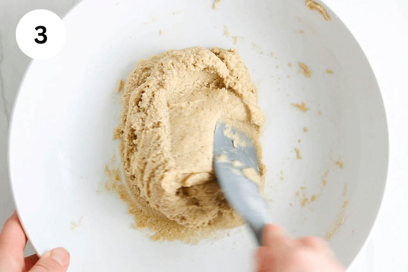A spatula mixing a thick cookie dough in a bowl.