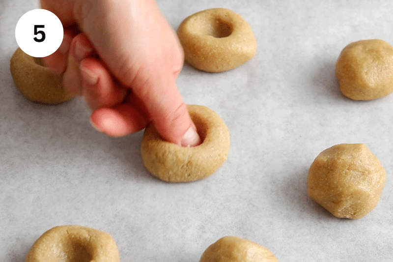 A thumb pressing on a ball of cookie dough.