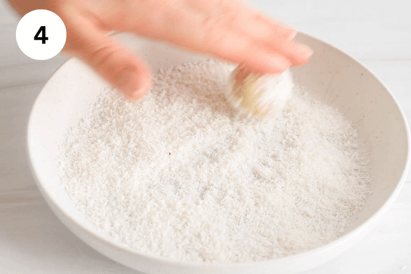 A hand rolling bliss balls in shredded coconut.