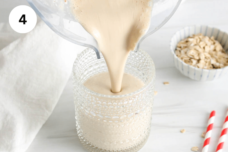 A blender pouring a creamy smoothie into a short glass.