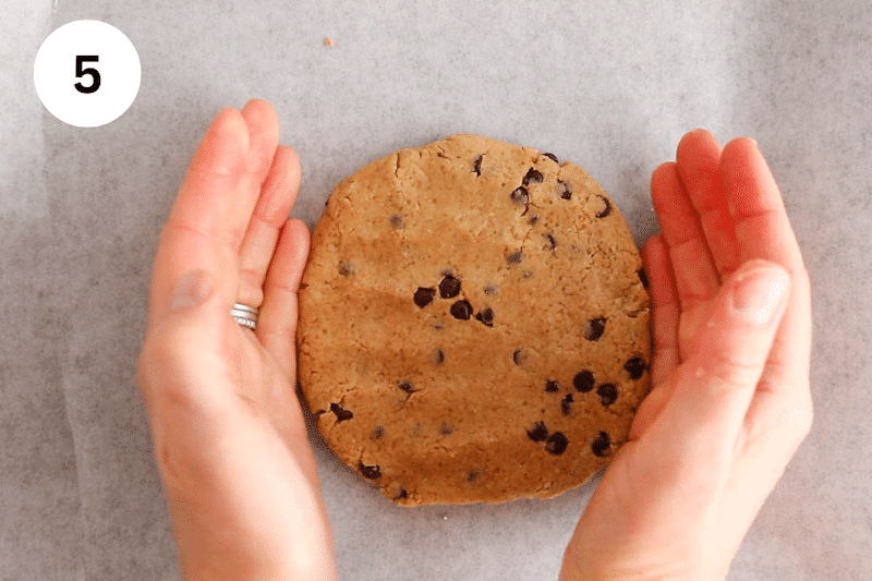 2 hands shaping some dough into a large cookie over parchment paper.