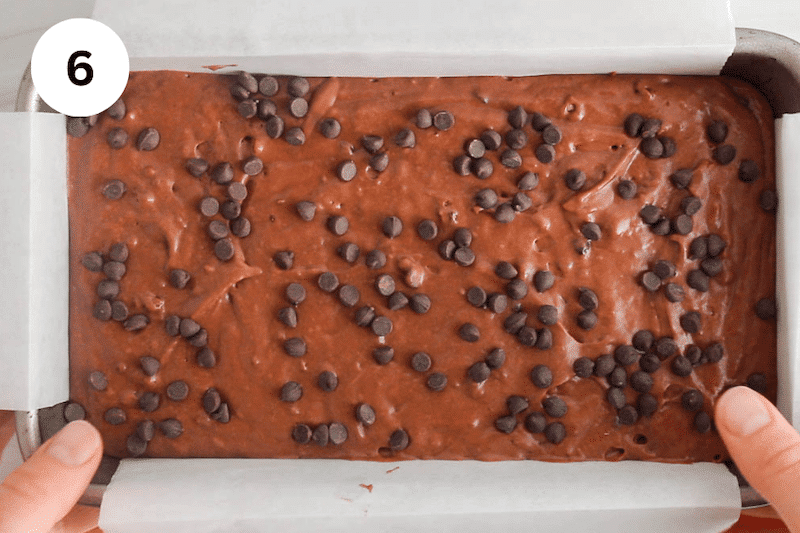 A chocolate cake batter in a loaf pan covered with chocolate chips.