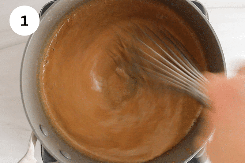 A large whisk stirring in a small pot with a peanut butter sauce.