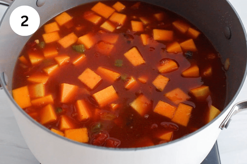 Large pot filled with tomato broth and squash.