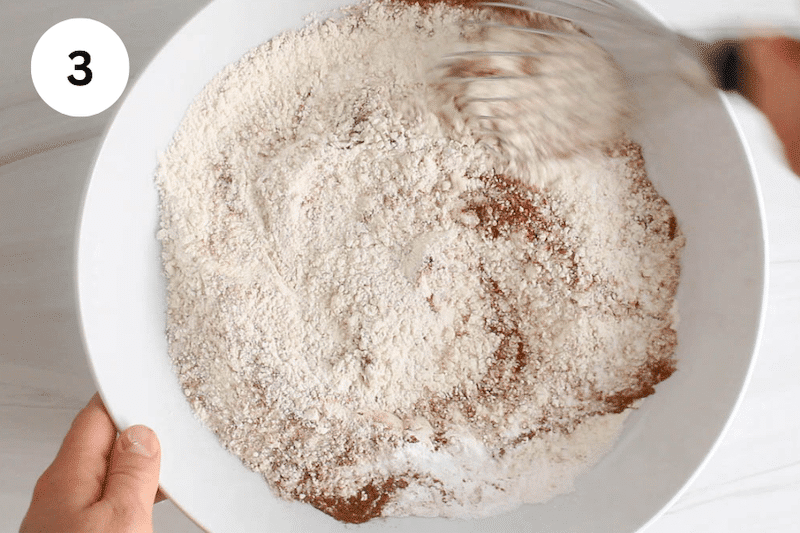 Flour and cinnamon in a large bowl with a whisk stirring.