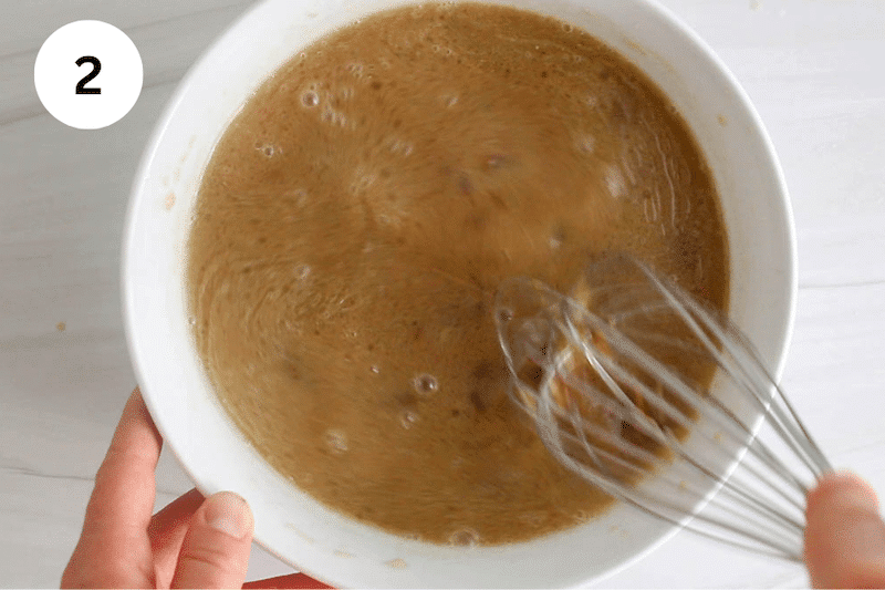A large whisk stirring in a bowl with milk and oil.