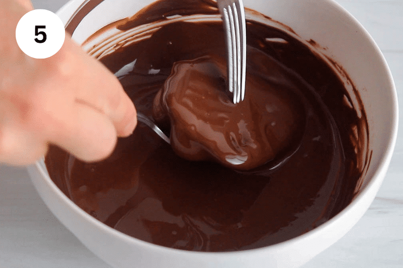 Forks dipping a yogurt cluster in chocolate.
