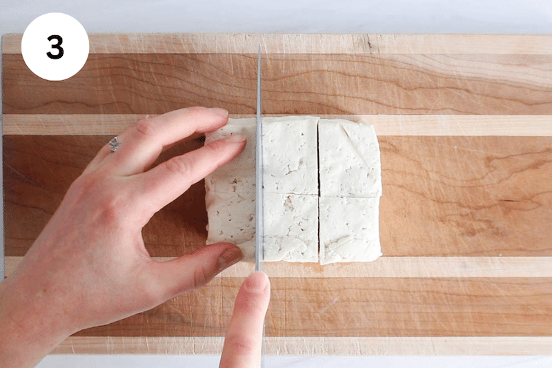 A knife slicing the tofu in large cubes.