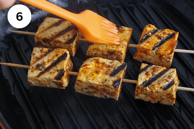 A cast iron pan with tofu skewers grilling over.