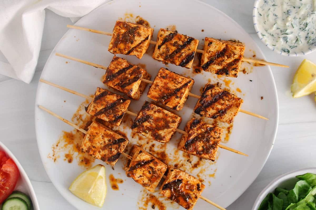 Vegan tofu souvlaki on a skewer on a white plate.