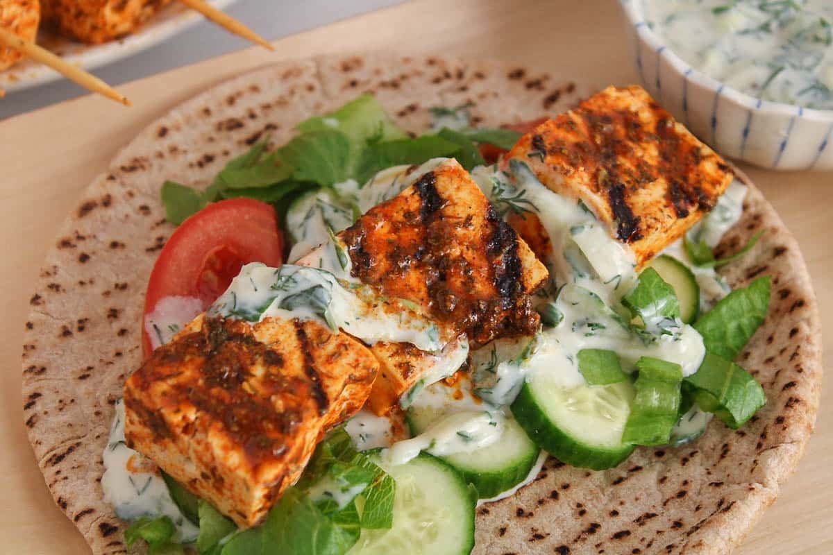 Saucy vegan tofu souvlaki with grilled line in a gyro with tzatziki sauce.
