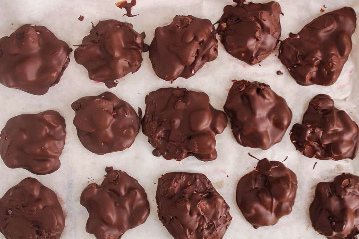 A few frozen chocolate covered strawberry yogurt clusters on parchment paper.