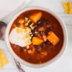 Bowl of warm black bean butternut squash soup topped with vegan sour cream and a side of crushed tortilla chips.