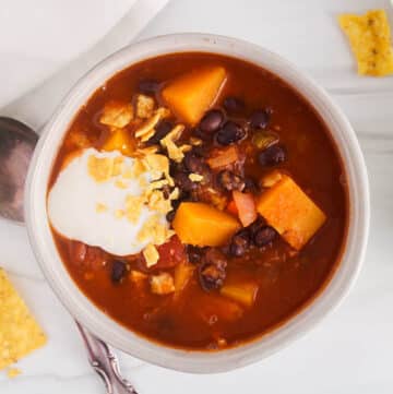 Bowl of warm black bean butternut squash soup topped with vegan sour cream and a side of crushed tortilla chips.