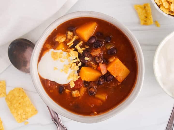 Bowl of warm black bean butternut squash soup topped with vegan sour cream and a side of crushed tortilla chips.