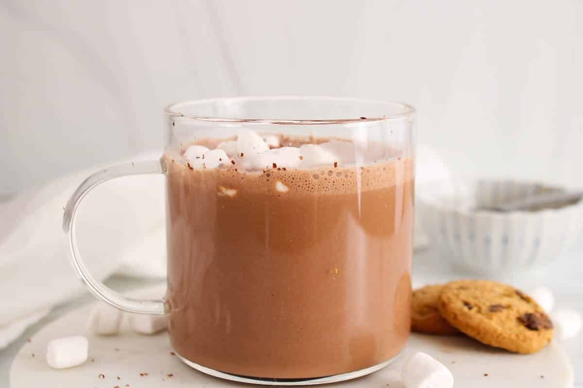 A small mug of protein hot chocolate with cookies in the background.